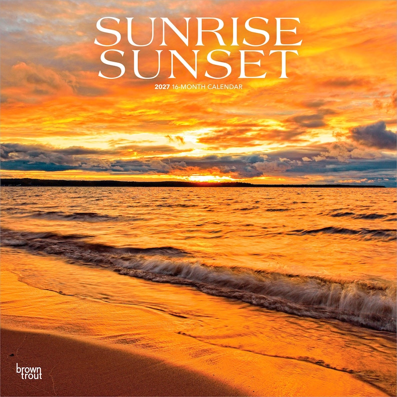 May include: A 2027 16-month calendar titled SUNRISE SUNSET. The cover features a vibrant photograph of a golden orange sunset over a calm ocean with gentle waves washing onto a sandy beach. The text BrownTrout is printed in the bottom left corner.