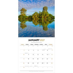May include: A wall calendar for January 2027 featuring a landscape photograph of green trees reflecting in calm blue water under a cloudy sky. The calendar grid displays the month, year, days of the week, and dates in black and gold text.