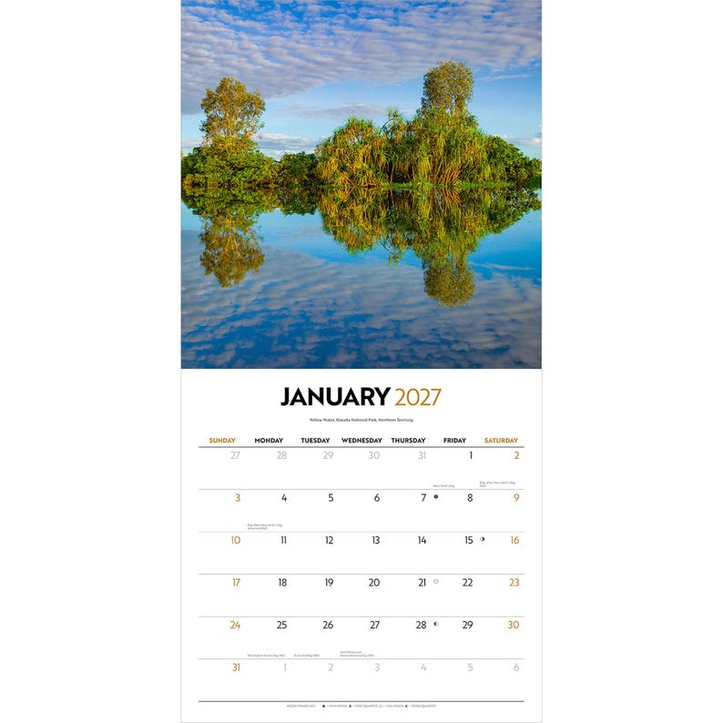 May include: A wall calendar for January 2027 featuring a landscape photograph of green trees reflecting in calm blue water under a cloudy sky. The calendar grid displays the month, year, days of the week, and dates in black and gold text.