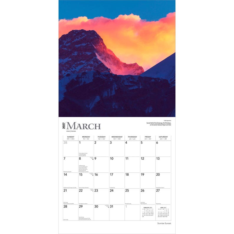 May include: A 2027 wall calendar for the month of March featuring a photograph of a snow-capped mountain peak at sunset with vibrant orange and pink clouds above. The calendar grid displays dates from the 1st to the 31st with black text on white.