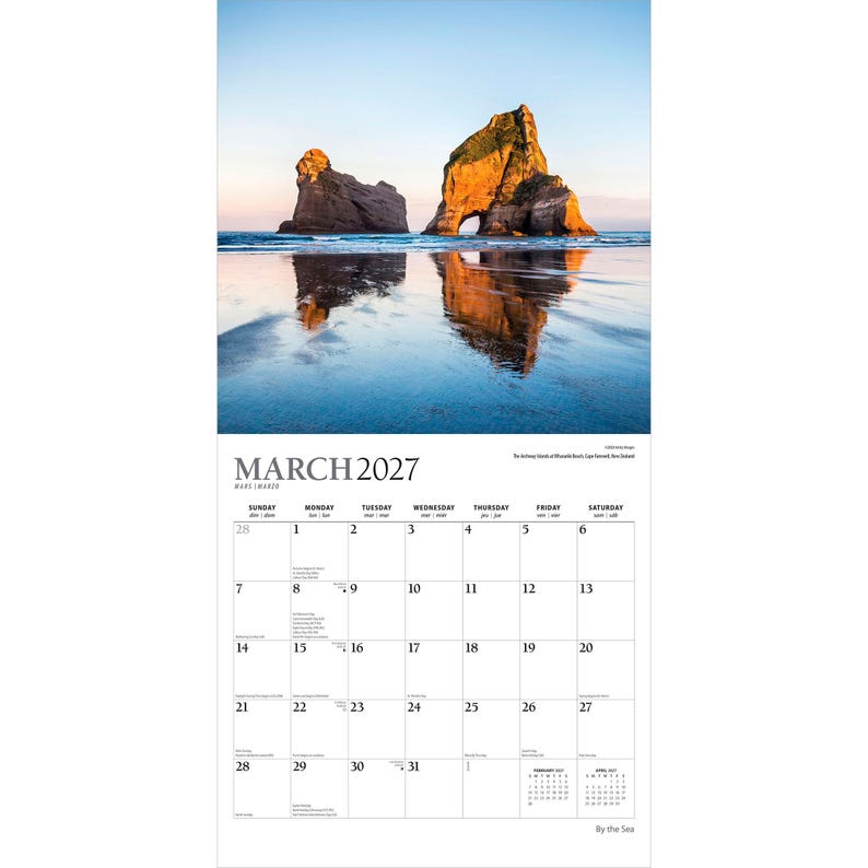 May include: A wall calendar for March 2027 featuring a photograph of two large rock formations on a beach at sunset. The image shows the rocks reflecting in the wet sand. The calendar grid displays the days of the month with clear black text.