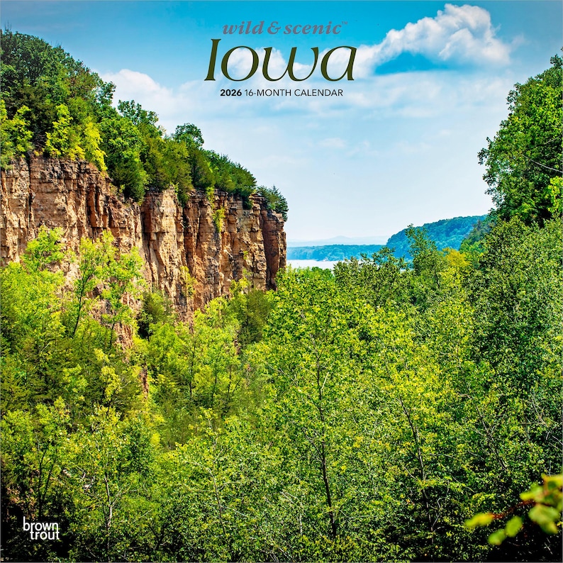 May include: A 2026 16-month calendar with a scenic Iowa landscape. The image displays a vibrant green forest, a tall rock cliff, and a blue sky with clouds. The words "wild & scenic" and "Iowa" are printed at the top of the calendar.