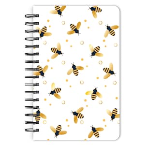May include: A white notebook with a gold and black bee pattern. The notebook has a spiral binding and is perfect for taking notes or journaling.