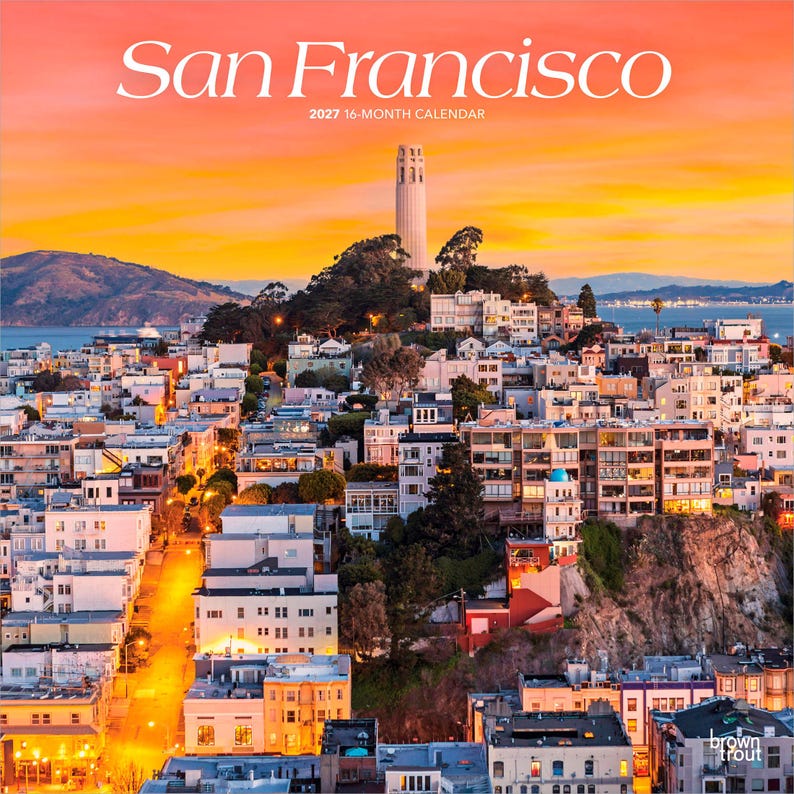May include: A 2027 16-month calendar titled San Francisco featuring a photograph of the city skyline at sunset. Coit Tower stands prominently on a hill above dense residential buildings, illuminated by a vibrant orange and yellow sky.