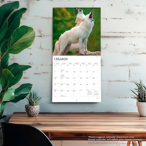 May include: A wall calendar for March 2023 featuring a photograph of two white wolves howling against a blurred green forest background. The calendar grid displays the days of the month with clear black text on a white background, including small calendars for February and April 2023.