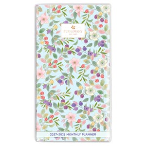 May include: A rectangular 2027-2028 monthly planner with a light blue cover featuring a botanical pattern of pink flowers, green leaves, and purple berries. A white rectangular label in the center displays the text TURNOWSKY EST. 1940.