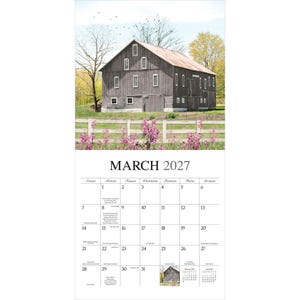 K&ouml;nnte beinhalten: Ein Wandkalender f&uuml;r M&auml;rz 2027 mit einer Fotografie einer verwitterten grauen Holzscheune hinter einem wei&szlig;en Lattenzaun und rosa Wildblumen. Das Kalenderraster zeigt den Monat, das Jahr und die Tage mit kleinem Text f&uuml;r Feiertage.
