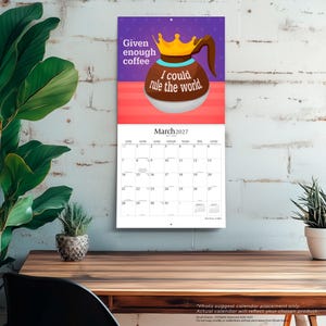 K&ouml;nnte beinhalten: Ein Wandkalender f&uuml;r M&auml;rz 2027 mit einer Grafik einer braunen Kaffeekanne, die eine goldene Krone tr&auml;gt. Der Text lautet, Given enough coffee I could rule the world. Das Kalenderraster zeigt die Tage des Monats vor einem violetten und roten Hintergrund.