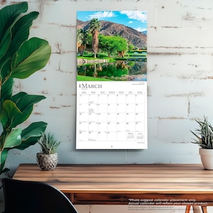 May include: A wall calendar for March 2023 featuring a landscape photograph of a pond reflecting palm trees and mountains under a blue sky. The calendar grid displays the days of the month with small text for the previous and following months.