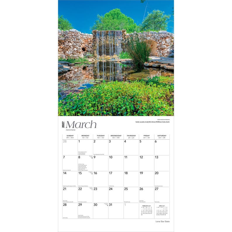 May include: A 2027 wall calendar for the month of March featuring a photograph of a stone waterfall cascading into a pond surrounded by lush green foliage. The calendar grid displays the days of the month with clear black text on a white background.