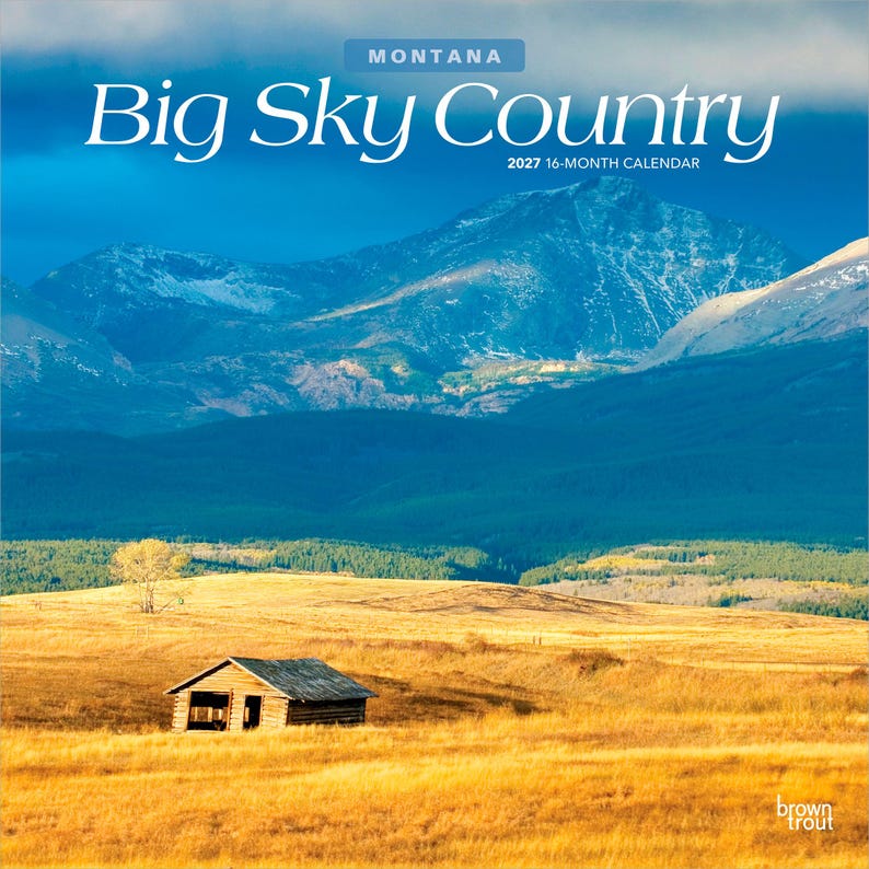 K&ouml;nnte beinhalten: Ein 16-Monats-Kalender f&uuml;r 2027 mit dem Titel Montana Big Sky Country, der eine Landschaftsaufnahme einer kleinen Holzh&uuml;tte auf einem goldenen Grasfeld unter einem weiten blauen Himmel und gro&szlig;en, dunklen, schneebedeckten Bergen zeigt.