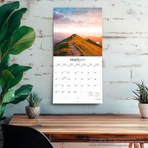 Puede incluir: Un calendario de pared para marzo de 2027 con una fotograf&iacute;a de paisaje de una cresta de monta&ntilde;a cubierta de hierba al atardecer. La cuadr&iacute;cula del calendario muestra los d&iacute;as del mes con el texto "March 2027" y una cita de Marcus Tullius Cicero.
