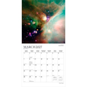 Op de afbeelding: Een wandkalender voor maart 2027 met een levendige afbeelding van een ruimtenevel met wervelende wolken van groen, oranje en rood gas, heldere sterren en een standaard rasterindeling met dagen en datums in zwarte tekst op een witte achtergrond.