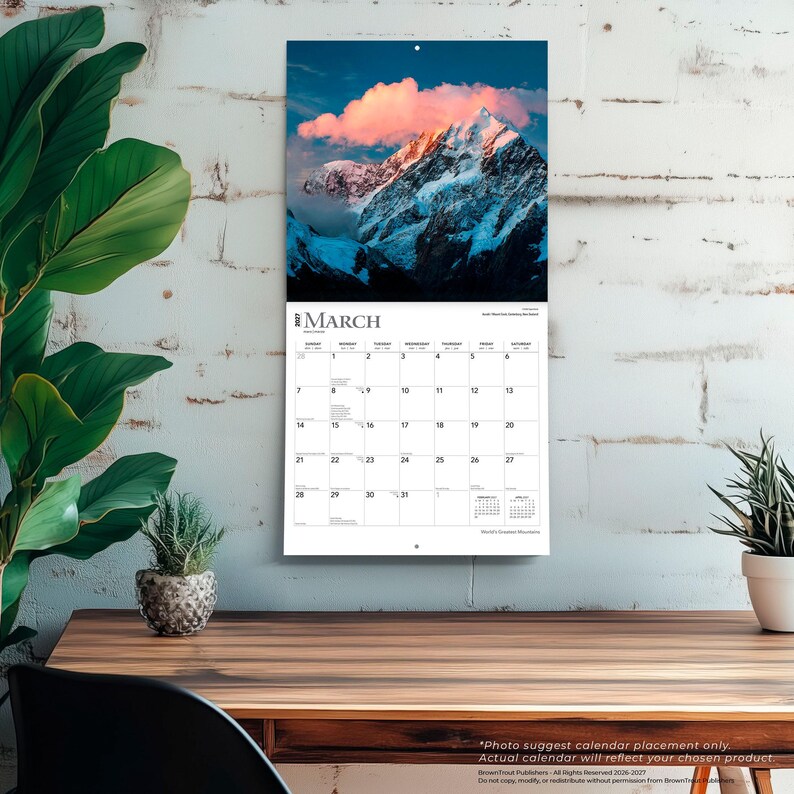 K&ouml;nnte beinhalten: Ein Wandkalender f&uuml;r M&auml;rz 2027 mit einer Fotografie eines schneebedeckten Berggipfels unter einem Sonnenuntergangshimmel mit rosa Wolken. Das Kalenderraster zeigt die Tage des Monats in schwarzer Schrift auf wei&szlig;em Hintergrund.