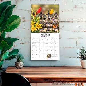 Puede incluir: Un calendario de pared para marzo de 2026 con una imagen vibrante de p&aacute;jaros posados en una valla decorativa entre flores. El calendario muestra los d&iacute;as del mes e incluye el texto "MARZO mars 2026".