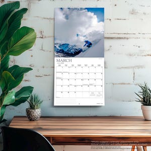 Peut inclure: Calendrier mural de mars 2024 avec un skieur en bleu sur une pente de montagne enneig&eacute;e sous un ciel nuageux. Le calendrier a un fond blanc avec une grille de dates et le mot "MARS".