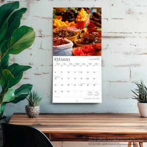 May include: A wall calendar featuring a vibrant image of a market scene with various spices and produce. The calendar page shows the month of March with the word "MARZO" at the top. The calendar is hanging on a white brick wall.