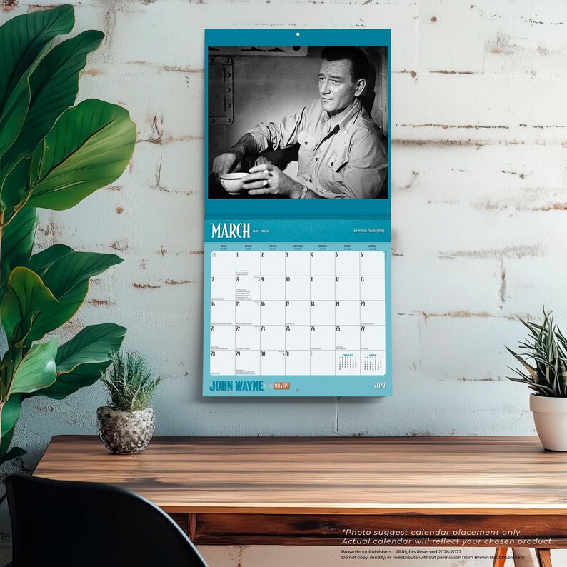 May include: A wall calendar featuring a black and white image of John Wayne. The calendar has a teal border and the month of March is displayed. The words "JOHN WAYNE" are printed at the bottom.