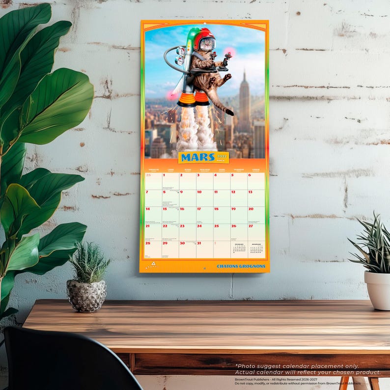 May include: A wall calendar for the month of March featuring a cat wearing a red helmet and a jetpack flying over a city skyline. The calendar grid displays the days of the month with the text MARS and CHATONS GROGNONS printed on the page.