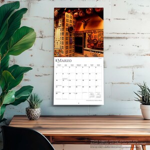 May include: A wall calendar for the month of March 2027 featuring a photograph of a rustic kitchen with patterned tiles, copper cookware, and a crucifix on the wall. The calendar grid displays the days of the month with the title MARZO at the top.