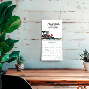 Pode incluir: Um calend&aacute;rio de parede para mar&ccedil;o de 2027 com uma ilustra&ccedil;&atilde;o em aguarela de uma colina com &aacute;rvores e um sol vermelho. O texto diz: Expect this to be a day of Healing, Awareness, Harmony and Gentle Order. A grelha mostra as datas.