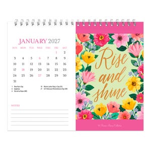 May include: A spiral-bound January 2027 calendar featuring a floral design on the right page with the text Rise and shine in gold script. The left page displays the calendar grid, the month, and a notes section with lines at the bottom.