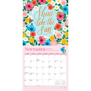 May include: A wall calendar for November 2027 featuring a light blue background with colorful floral illustrations and butterflies. The top section displays the gold cursive text Shine like the sun. The bottom section shows a monthly grid.