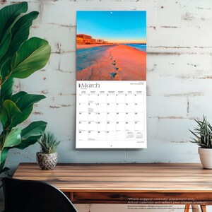 May include: A wall calendar for March 2023 featuring a photograph of a sandy beach at sunset with footprints leading towards the ocean. The calendar grid displays the days of the month in black text on a white background with a clean, organised layout.