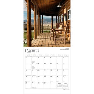 K&ouml;nnte beinhalten: Ein Wandkalender f&uuml;r M&auml;rz 2027 mit einem Foto einer Holzveranda mit zwei rustikalen St&uuml;hlen vor einer Berglandschaft. Das Kalenderraster zeigt die Tage des Monats mit deutlicher schwarzer Schrift auf einem wei&szlig;en Hintergrund.