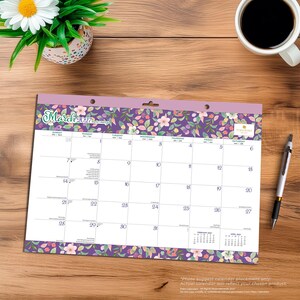 May include: A March 2027 wall calendar featuring a purple floral pattern border with green leaves and pink flowers. The calendar grid displays days of the week and dates, with small February and April 2027 calendars in the bottom right corner.