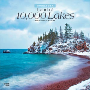 May include: A 2027 16-month calendar titled Minnesota Land of 10,000 Lakes. The cover features a winter landscape with a rocky, snow-covered shoreline, evergreen trees, and icy blue water meeting a reddish-brown pebble beach under a cloudy sky.