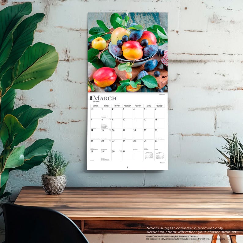Puede incluir: Un calendario de pared para marzo de 2027 con una fotograf&iacute;a de un cuenco lleno de melocotones frescos, ciruelas y hojas verdes. La cuadr&iacute;cula del calendario muestra el mes, los d&iacute;as de la semana y las fechas en blanco y negro sobre papel blanco.