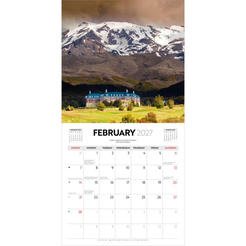 May include: A wall calendar for February 2027 featuring a photograph of a large multi-story building with a blue roof situated in a grassy field before a snow-capped mountain range under a cloudy sky. The calendar grid displays dates and text.