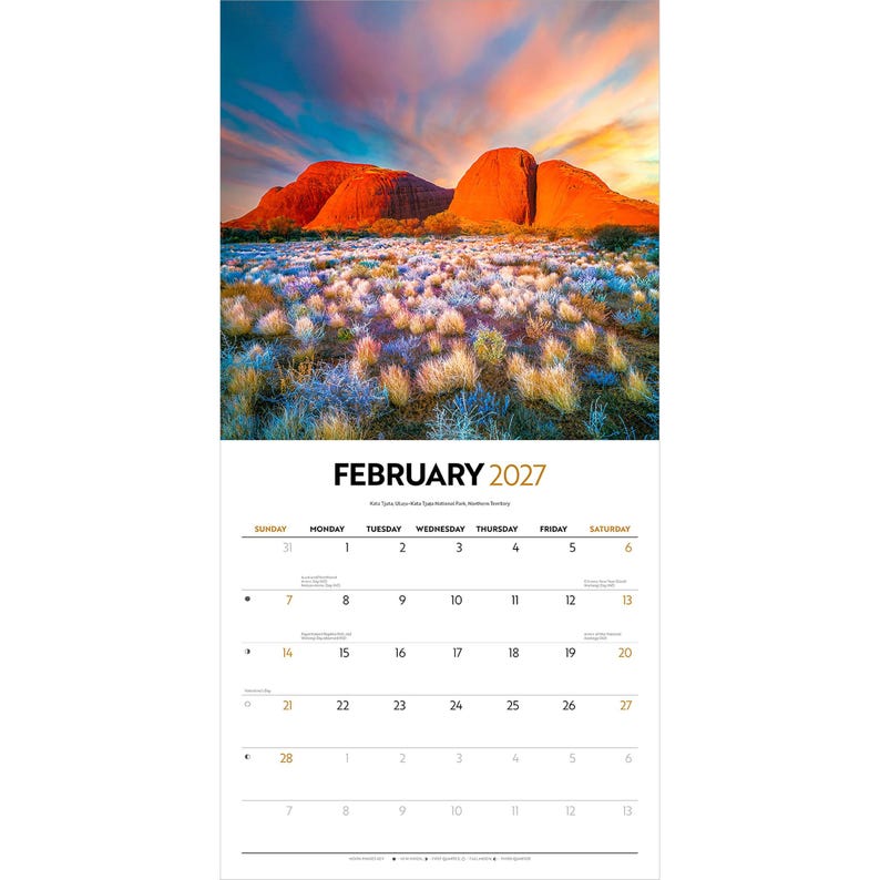 May include: A wall calendar for February 2027 featuring a landscape photograph of red rock formations under a vibrant sunset sky. The foreground displays low-lying desert vegetation with blue and gold tones. The calendar grid lists days of the week.