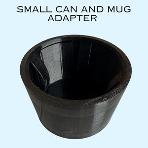 Peut inclure: Un adaptateur cylindrique noir avec un dessus évasé, conçu pour contenir une petite canette ou un mug. Le texte "SMALL CAN AND MUG ADAPTER" est imprimé au-dessus de l'objet. L'adaptateur a une surface texturée et un intérieur lisse et sombre.