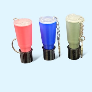May include: Three keychain-sized cups with lids, each in a different color: pink, blue, and gray. The cups have a black base and a silver chain attached.
