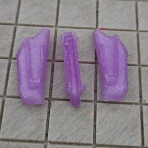 Może przedstawiać: Trzy małe, lawendowe kawałki plastiku ułożone są na kafelkowanej powierzchni. Dwa kawałki mają podobny kształt, a trzeci jest prostokątny. Kawałki mają teksturowany wygląd.