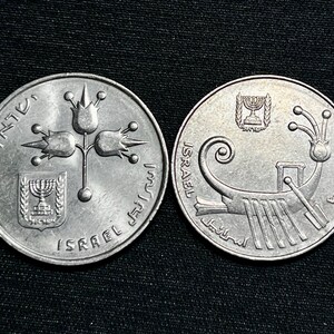 Puede incluir: Dos monedas israelíes de plata. Una moneda presenta un diseño floral con la Estrella de David y texto en hebreo. La otra moneda muestra un barco con texto en hebreo y la palabra "Israel". Ambas monedas están sobre un fondo oscuro.