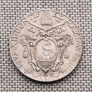 May include: A silver-coloured circular coin featuring the text PIVS XII PONTIF EX MAXIMVS AN III and the date 1941. The centre displays a shield with a bird above three mounds and waves, topped by a papal tiara and crossed keys of Saint Peter.