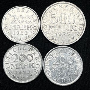 May include: Four silver German coins from 1923, featuring the text "DEUTSCHES REICH" and "MARK". Two coins are marked "200", and one is marked "500". The coins are displayed against a black backdrop.