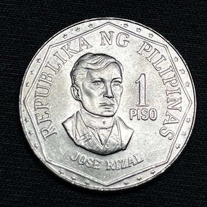 Op de afbeelding: Een zilveren 1 Piso munt uit de Filipijnen. De munt toont een portret van Jose Rizal, de denominatie "1 PISO" en de tekst "REPUBLIKA NG PILIPINAS". De munt heeft een gedetailleerd ontwerp en een glanzende afwerking.