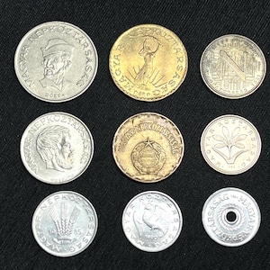 May include: A collection of nine vintage Hungarian coins, featuring various designs and inscriptions. The coins are in silver and gold tones, with visible details of historical figures and symbols. The coins are arranged on a dark surface.