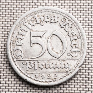 Puede incluir: Una moneda de plata de 50 Pfennig de 1922. La moneda presenta el texto "Deutsches Reich" en el borde superior, con el número "50" en un lugar destacado. La palabra "Pfennig" está escrita debajo del número, y el año "1922" en la parte inferior.