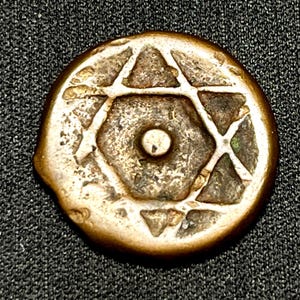 Peut inclure: Une pièce de monnaie ronde et antique avec un motif d'étoile de David au centre. La pièce a un bord de couleur bronze et une surface usée et texturée. L'étoile est composée de triangles entrecroisés et d'un cercle central.