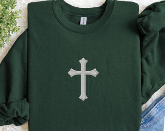 May include: A dark green sweatshirt with a silver embroidered cross design centered on the front. The sweatshirt has a crew neck and long sleeves. The cross is detailed with decorative edges.