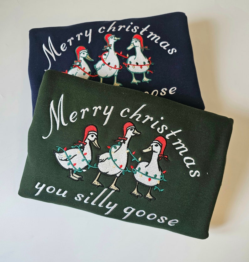 May include: Two sweatshirts with a Christmas theme. The top sweatshirt is navy blue with white text that says "Merry Christmas" and a line of geese wearing Christmas lights. The bottom sweatshirt is dark green with white text that says "Merry Christmas you silly goose" and a line of geese wearing Christmas lights.