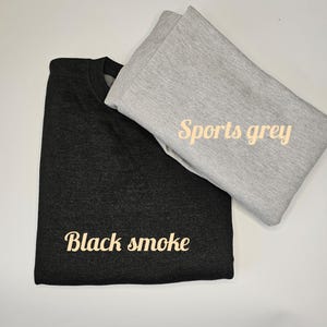 May include: Two folded sweatshirts, one black with the text "Black smoke" and one gray with the text "Sports grey".
