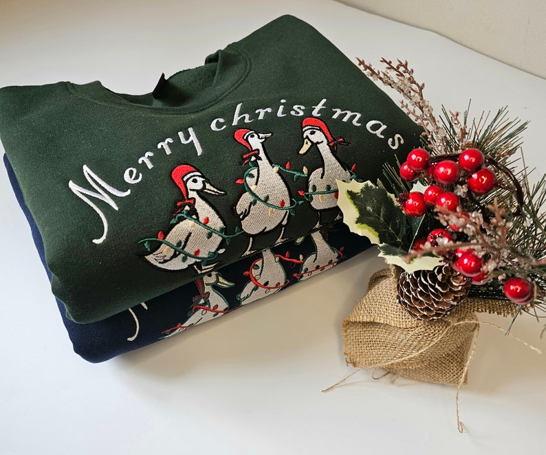 May include: A green sweatshirt with the text "Merry Christmas" embroidered on the front. The sweatshirt features a design of five geese wearing Santa hats and carrying Christmas lights.