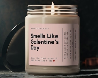 May include: A lit soy candle in a glass jar with a silver lid. The label reads "Smells Like Galentine's Day" with text about the scent and origin. The candle is hand-poured and crafted in California.