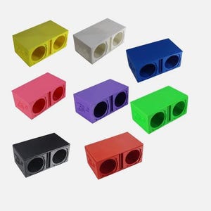 Puede incluir: Una colección de cajas de altavoces rectangulares y coloridas en varios tonos, incluyendo amarillo, blanco, azul, rosa, morado, verde, negro y rojo. Cada caja tiene dos aberturas circulares.